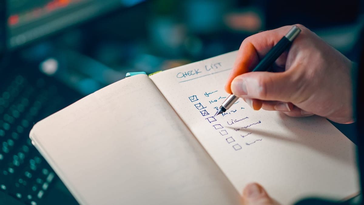 A handwritten checklist on a notepad beside a pen
